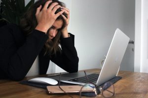 woman clutching head working on laptop