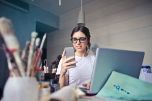 woman holding cellphone while sitting at laptop